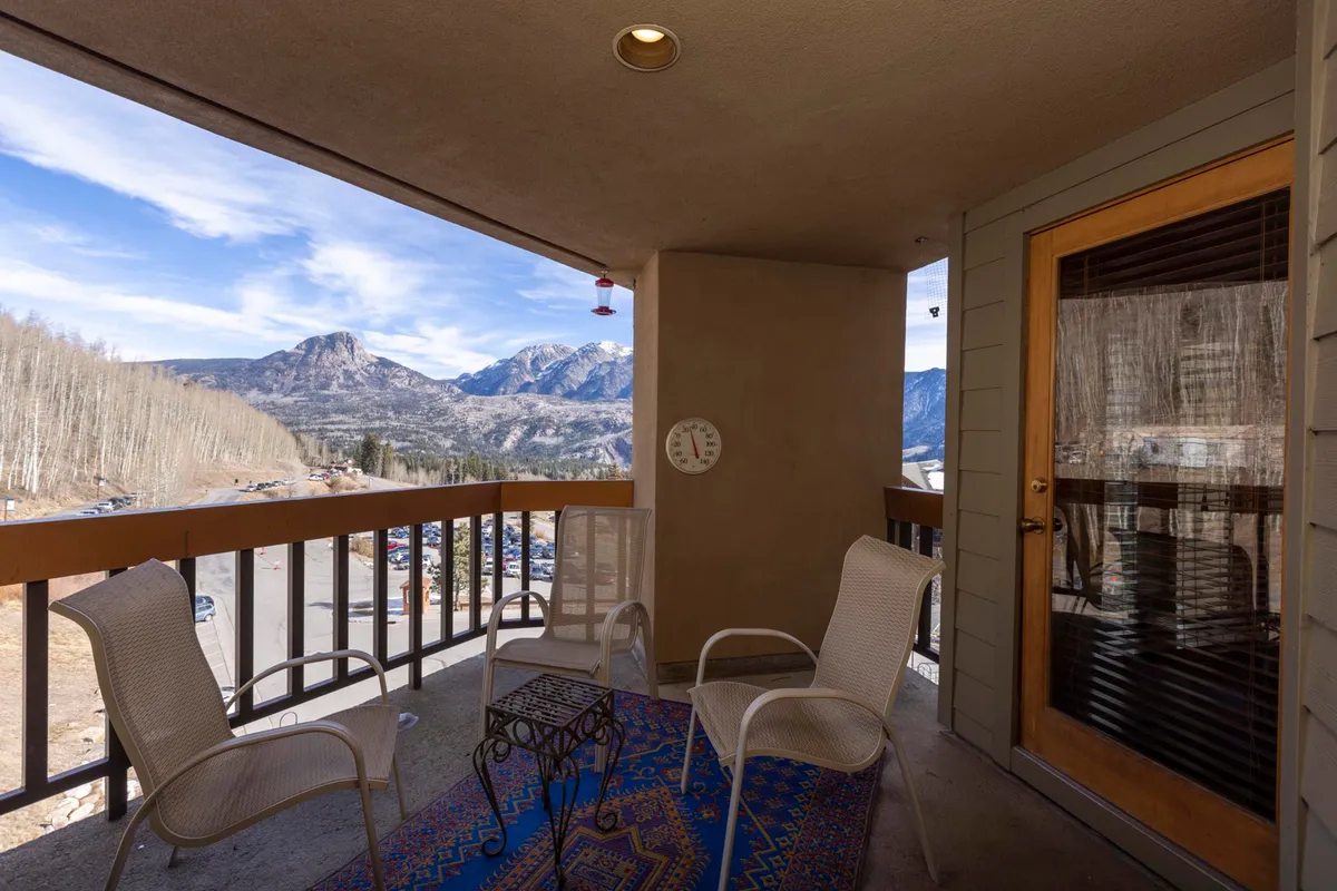 An inviting outdoor patio furnished with comfortable seating and a decorative rug, set against the backdrop of scenic mountains. The glass door connects the patio to the interior, suggesting easy flow between indoor comfort and outdoor leisure. The space is ideal for family gatherings or quiet moments enjoying the view.