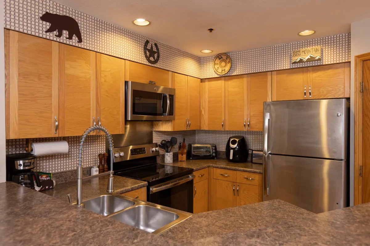 A cozy kitchen scene featuring sleek stainless steel appliances, rich wood cabinetry, and tasteful wall art. The layout is designed for efficient meal prep and group cooking, emphasizing function as well as style.