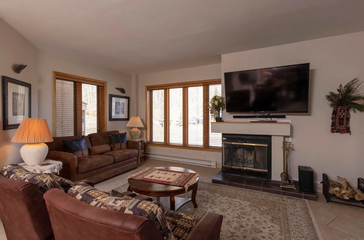A cozy interior living space featuring a comfortable sofa, crackling fireplace, large windows, and a decorative table. The room feels inviting and intimate, perfect for couples relaxing together after a day of exploring.