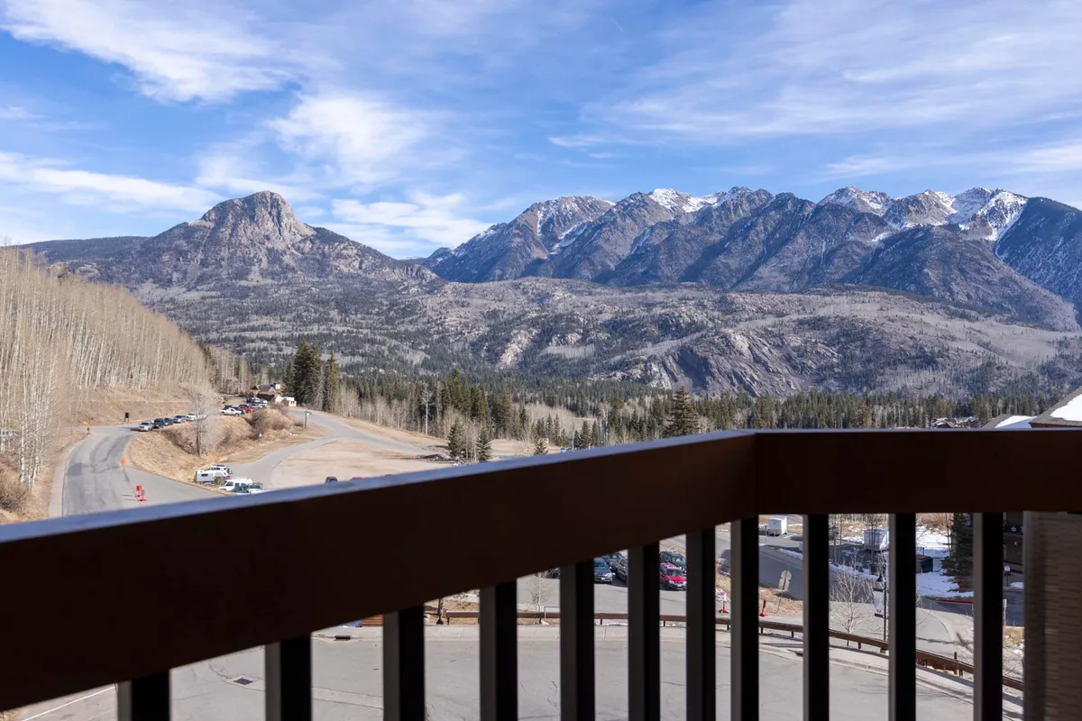 A breathtaking view of a mountain range and valley framed by a tree line. The scene suggests early morning light with potential for sunrise or the serene beauty of stargazing at night. The winding road below hints at adventure, while the peaceful natural setting evokes a sense of intimacy and awe.