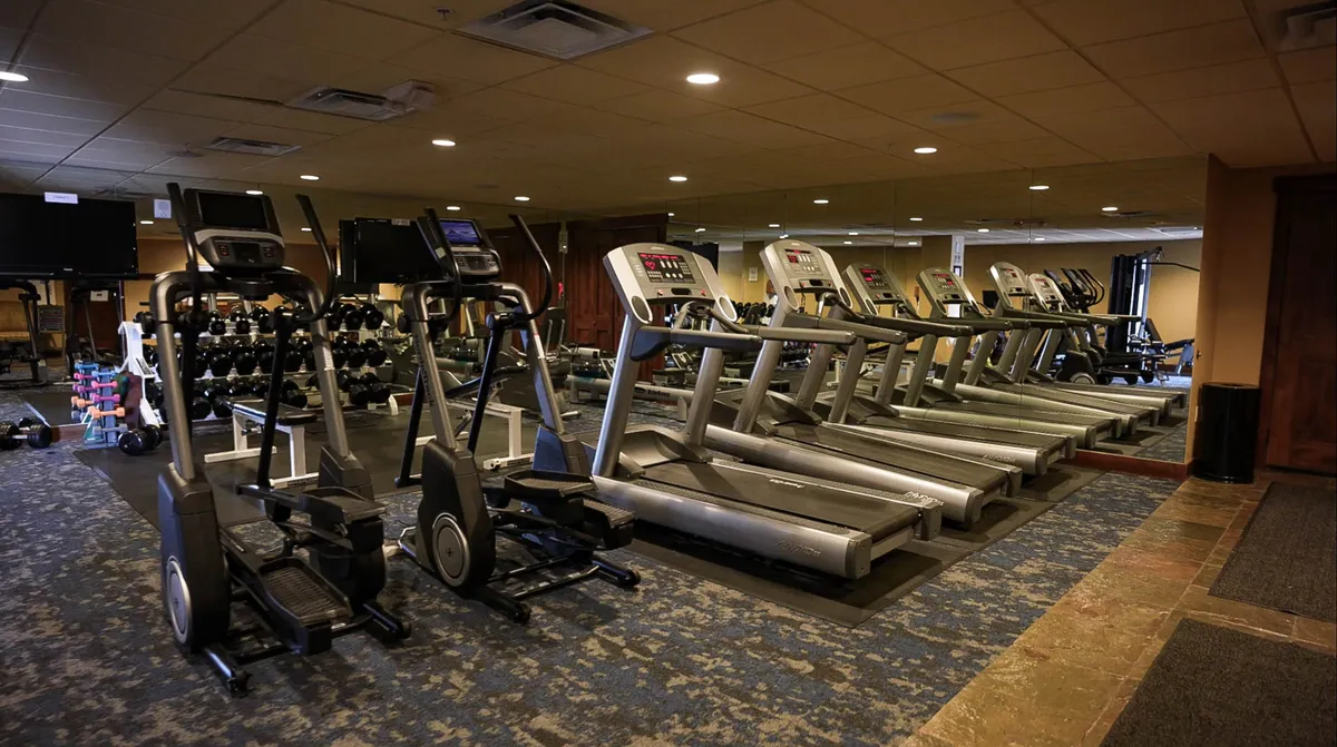 A modern, well-equipped fitness center with several treadmills, ellipticals, and free weights set against large windows. The bright, spacious layout encourages guests to keep up with their fitness routines while away from home.