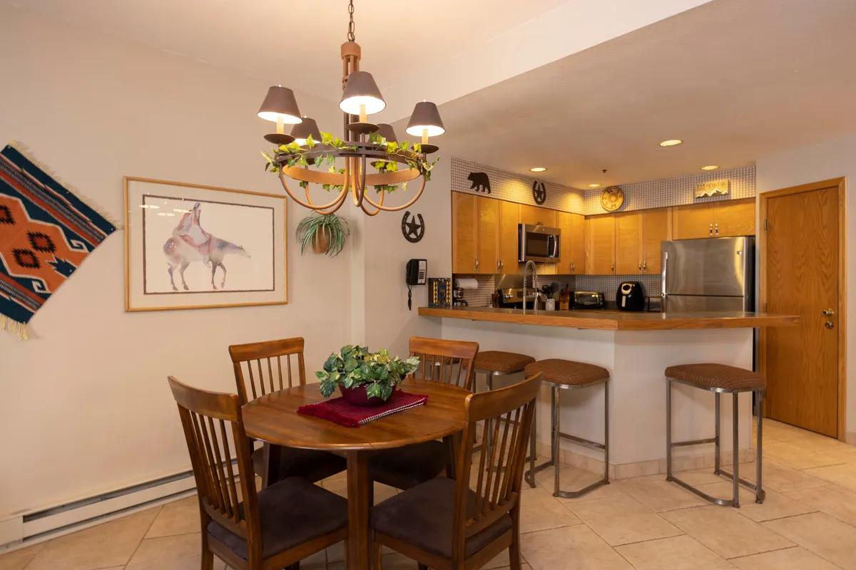A welcoming dining area featuring a sturdy table, elegant chandelier, adjacent kitchen, and decorative wall art. The setup is perfect for group meals or game nights, with a cozy, intimate ambiance that encourages connection.