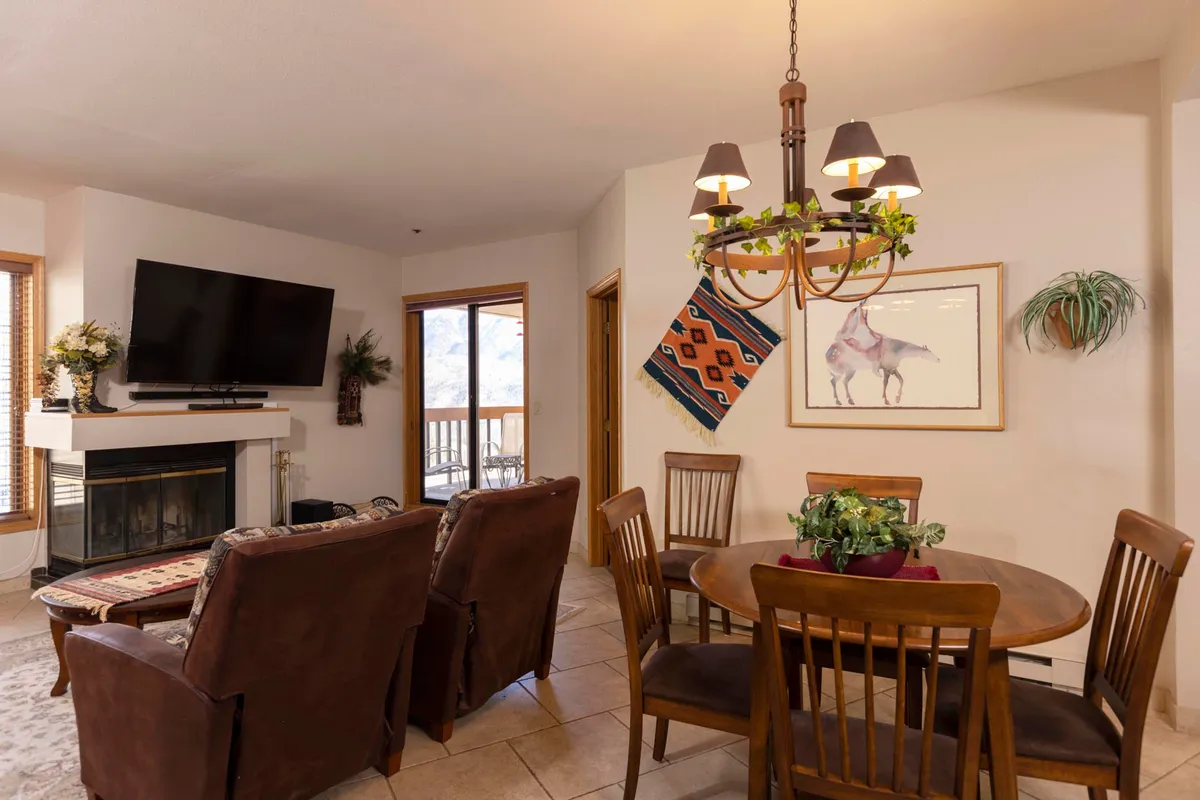 A spacious open-concept area combining a living room with a fireplace and a dining table, accented by tasteful wall art and large windows. This space showcases both relaxing lounge seating and a table set for group meals, with warm lighting enhancing the inviting mood.