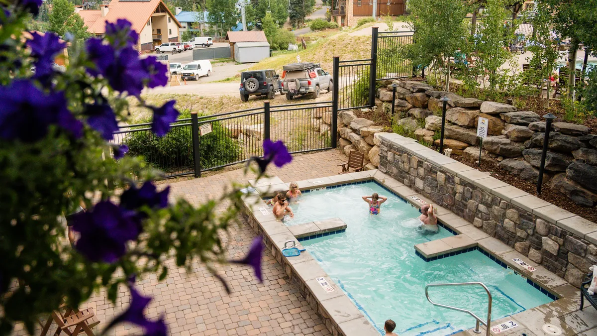 An inviting outdoor scene featuring a sparkling swimming pool and adjacent hot tub set amid lush flowers and mature trees. The area is designed for relaxation and socializing, with ample seating and natural scenery enhancing the resort-style vibe.